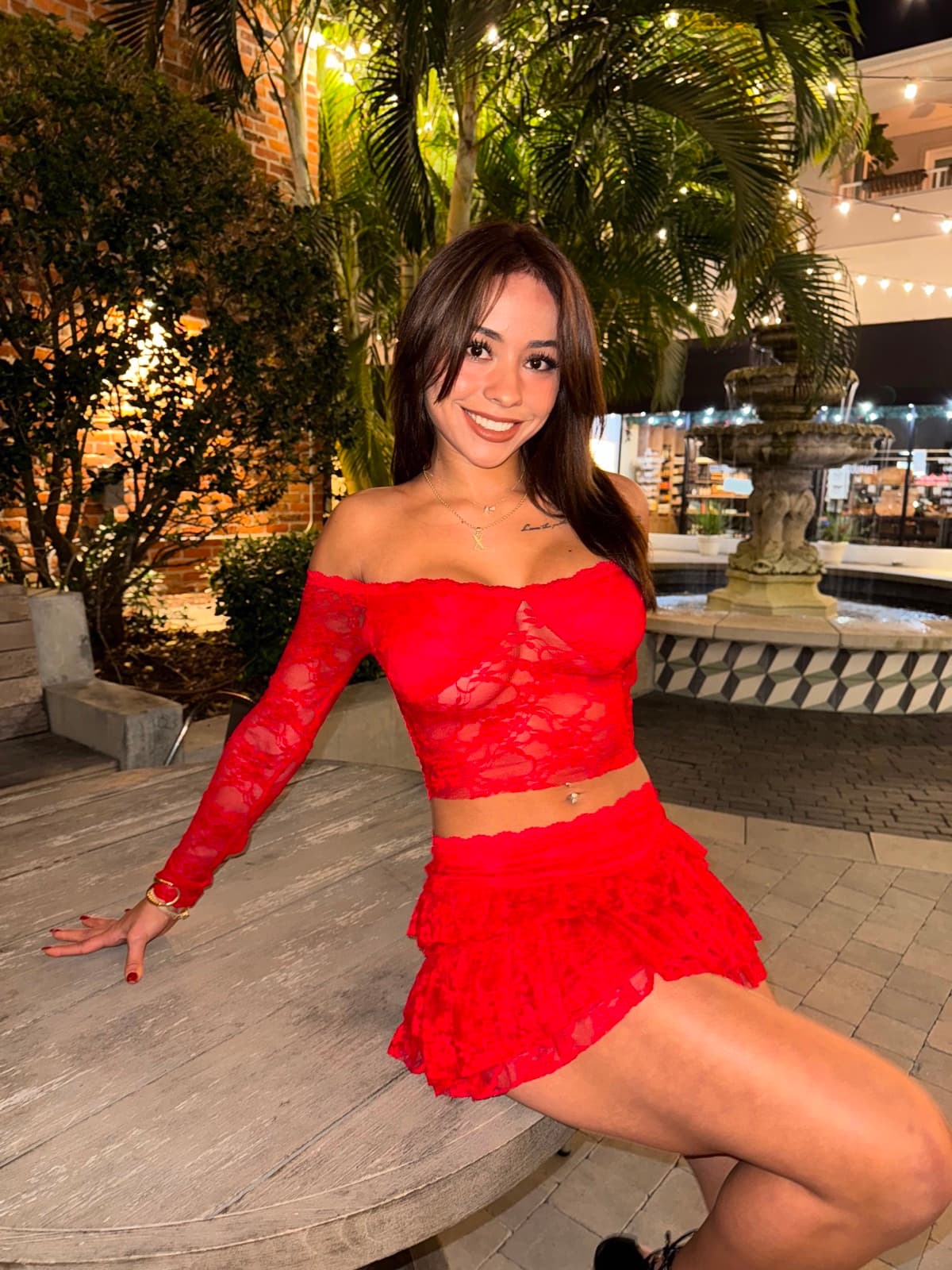 Ximena in a red lace set sitting by a fountain