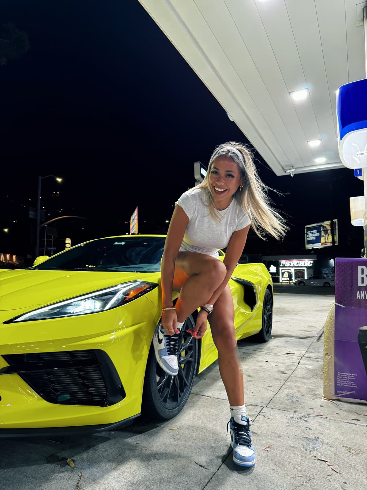Ximena at a gas station at night beside a yellow sports car